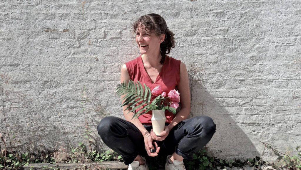 Anna Voss mit Keramik und Blumen vor weißer Mauer